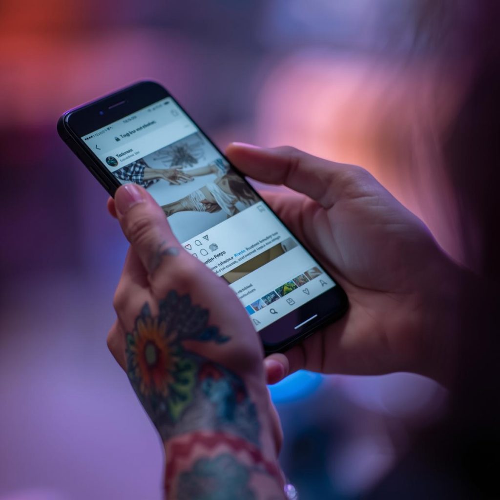 Photo illustrant quelqu'un tatoué avec un téléphone portable dans les mains. Sur son téléphone, il y a un réseau social.